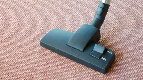 Ein Staubsaugeraufsatz reinigt einen Teppich und entfernt Staub, während er auf einem roten, strukturierten Boden steht.