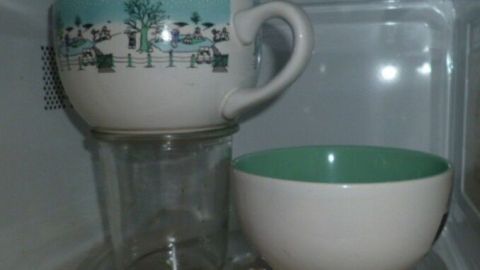 Eine Tasse steht über einem Glas in einer Mikrowelle, während eine Schüssel daneben platziert ist; ineffiziente Platznutzung.