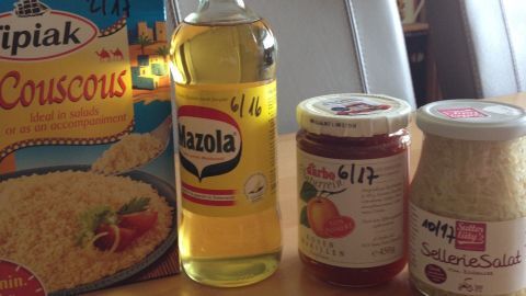 Auf einem Holztablett stehen eine Packung Couscous, eine Flasche Öl, zwei Gläser mit Marmelade und einen Salatdressing-Mix.