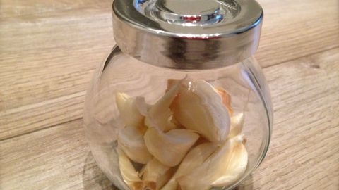 Ein Glas mit Knoblauchzehen steht auf einer Holzoberfläche und wird zur Aufbewahrung im Kühlschrank verwendet.