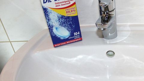 Ein Emaille Waschbecken steht im Badezimmer, daneben eine Verpackung für Gebissreiniger, die frisch und sauber wirkt.