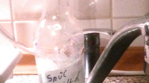 Eine Flasche mit Spülmittel steht neben einem Wasserhahn in einer Küche, bereit zum Dosieren beim Geschirrspülen.