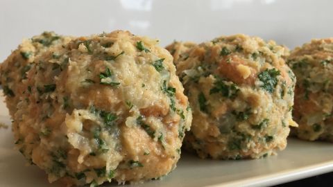 Semmelknödel liegen auf einem Teller, nah aufgenommen, mit Kräutern durchzogen, servierbereit im hellen Raum.