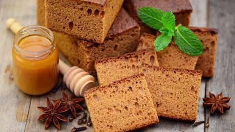 Braune Kuchen liegen zuschneiden auf einer Holzplatte, umgeben von Honig, Gewürzen und frischer Minze.