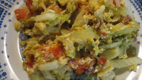 Rührei mit Tomaten und Zwiebeln auf einem blauen Muster-Teller arrangiert, appetitlich und farbenfroh präsentiert.