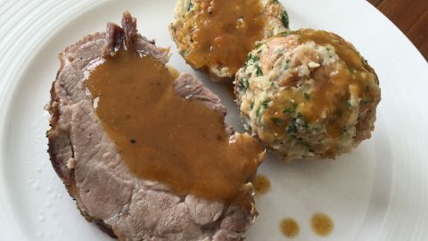 Saftiger Schweinebraten liegt auf einem weißen Teller, begleitet von zwei knusprigen Knödeln und reichlich Soße.