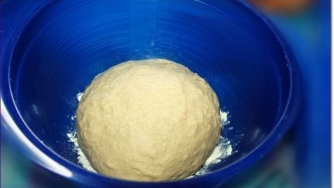 Ein Hefeteigball liegt in einer blauen Schüssel und wartet darauf, aufzugehen, um zubereitet zu werden.