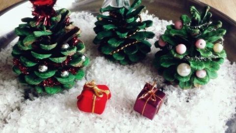 Deko Weihnachtsbäume aus Tannenzapfen stehen auf einer weißen Schneedecke, umgeben von kleinen Geschenken.