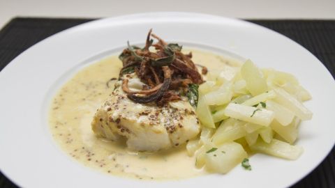 Ein Teller mit Kohlrabigemüse, das in einer sahnigen Sauce serviert wird, daneben gedämpfte Kohlrabi-Stücke.