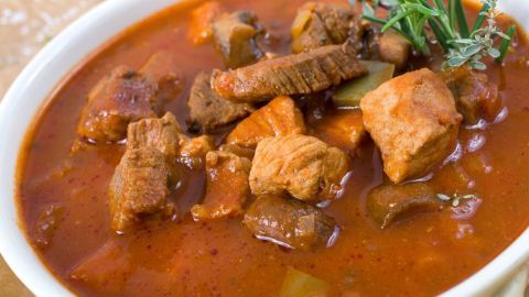 Ein aromatisches Rindergulasch liegt in einer weißen Schüssel, umgeben von einer rustikalen Tischdecke.