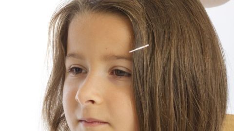Ein Mädchen mit langen Haaren erhält mit einem Kamm und einer Lupe eine Kopfläuseuntersuchung im stilvollen Raum.