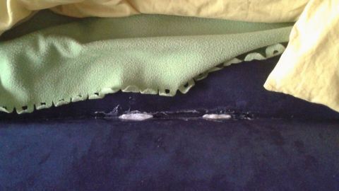 Ein Luftbett mit einem Riss liegt unter einer gelockten Bettdecke, während es in einem Schlafzimmer zur Reparatur wartet.