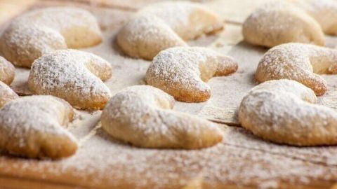 Leckere Vanillekipferl liegen auf einem Holzbrett, bestäubt mit Puderzucker, bereit zum Genießen.