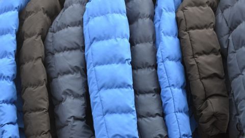 Dunkelblaue und schwarze Daunenjacken hängen ordentlich nebeneinander in einem Geschäft, bereit zum Verkauf oder zur Reinigung.