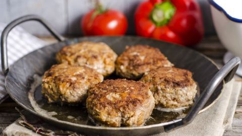 In einer Pfanne liegen saftig gebratene Frikadellen, umgeben von frischem Gemüse wie Tomaten und Paprika.