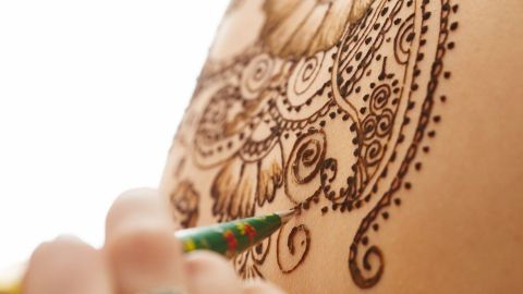 Eine Hand zeichnet ein kunstvolles Henna-Tattoo auf die Haut, um Haarverlust während der Chemotherapie zu kaschieren.