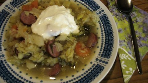 Ein großer Teller mit Wirsingtopf und Cabanossi wird appetitlich angerichtet, garniert mit einem Klecks Sahne.