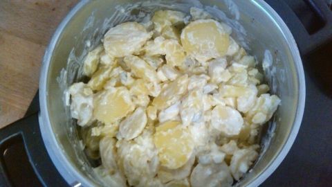 Ein Topf enthält cremigen Kartoffelsalat mit selbstgemachter Mayonnaise, auf einer Holzoberfläche platziert.