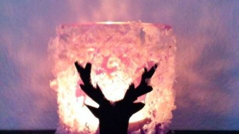 Ein Teelichtglas ist weihnachtlich mit einer Rentier-Silhouette verziert und strahlt warmes Licht in einem gemütlichen Raum.