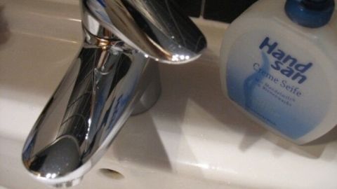 Ein glänzender Wasserhahn spiegelt sich über einem Waschbecken, neben einer Handwaschseife, um Kalkflecken zu vermeiden.