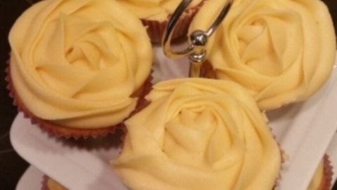 Sechs dekorative Cupcakes in Form von gelben Rosen stehen auf einem zweistufigen Teller in einer modernen Küche.