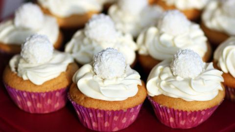 Muffins mit einer cremigen Topping-Schicht und einer süßen, runden Dekoration sind auf einem Platten arrangiert.