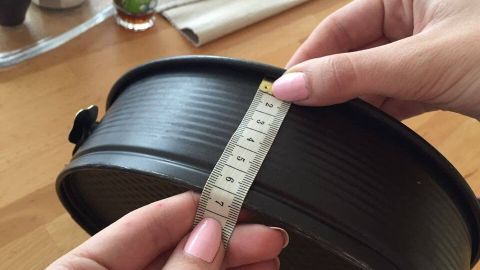 Eine Hand hält ein Maßband an einer Kuchenform, während sie die Größe überprüft, um einen perfekten Kuchen ohne Kuppe zu backen.