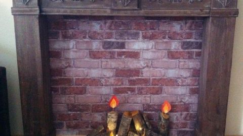 Holzscheit-Kerzen stehen auf einem rustikalen Kamin, umgeben von einer Backsteinwand und sanftem Licht.