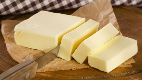 Eine frische Butter liegt auf einem Holzbrett, während ein Messer Stücke davon schneidet, um sie zu servieren.