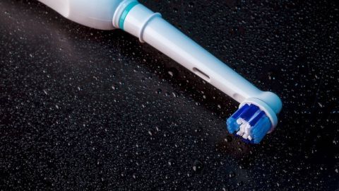 Eine elektrische Zahnbürste liegt auf einer dunklen Oberfläche, bereit zur Reinigung, während sie die Zahnpflege unterstützt.