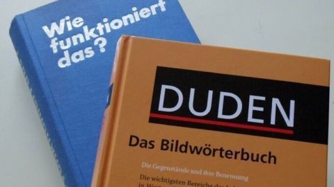 Zwei Bücher liegen auf einem Tisch: ein blaues mit der Frage "Wie funktioniert das?" und ein orangefarbenes Duden-Bildwörterbuch.