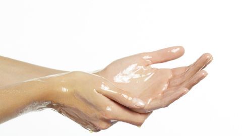 Eine Hand trägt eine feuchtigkeitsspendende Creme auf die andere Hand auf, um trockene Hände zu pflegen.
