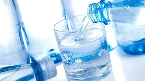 Eine Wasserflasche gießt frisches Wasser in ein Glas, umgeben von weiteren Flaschen und einer klaren Umgebung.
