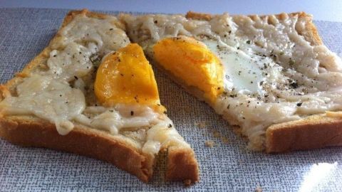 Knuspriger Toast mit geschmolzenem Käse und einem gebratenen Ei auf einer neutralen Oberfläche, appetitlich angerichtet.