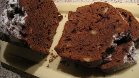Ein saftiger Quitten-Schoko-Kuchen mit Walnüssen liegt auf einem hellen Brett, in Stücke geschnitten, im hellen Umfeld.