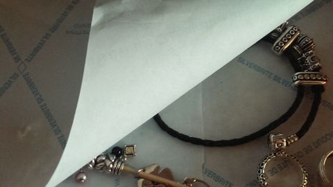 Ein silbernes Schmuckstück wird unter einem Schutzpapier präsentiert, um Anlaufen zu verhindern. Der Hintergrund ist neutral.