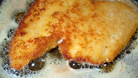 Ein goldbraun paniertes Schnitzel brät in einer Pfanne mit sprudelndem Fett, umgeben von blubbernden Blasen.