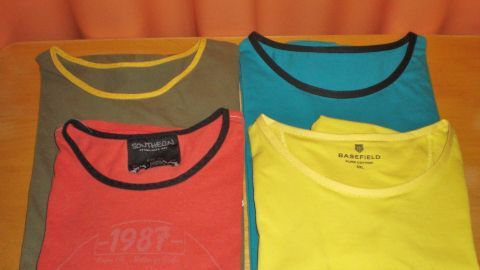 Vier T-Shirts mit unterschiedlichen Halsausschnitten und Farben liegen ordentlich auf einem Tisch, bereit für Anpassungen.