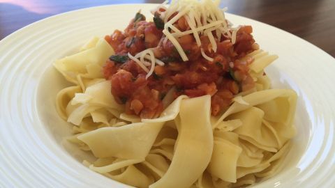 Eine Portion Bandnudeln wird mit einer herzhaften Linsen-Ragout-Sauce und geriebenem Käse serviert, auf einem weißen Teller.
