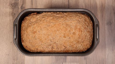 Ein frisch gebackenes Brot aus einer Mischung in einer Backform liegt auf einer Holzoberfläche.