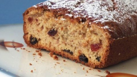Kuchenbrot mit Früchten liegt auf einem Teller, mit Puderzucker bestäubt und zeigt saftige Fruchtstücke im Inneren.