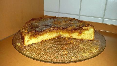 Ein Altbadischer Zimt-Zucker-Kuchen liegt angeschnitten auf einem Glasteller in einer Küchenecke mit Fliesen.
