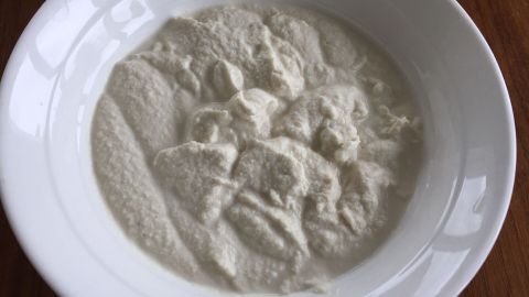 Eine Schüssel mit cremiger, veganer Cashew Sour Cream steht auf einem Holztisch und bietet eine glatte, weiße Textur.