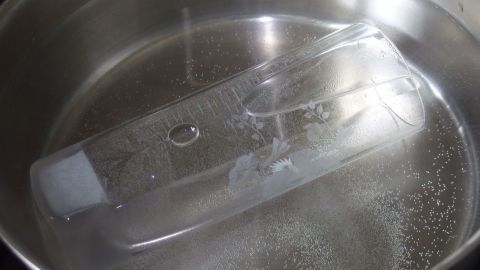 Ein durchsichtiger Kunststoffbehälter schwimmt in einem Topf mit kochendem Wasser, das sprudelnd ist.
