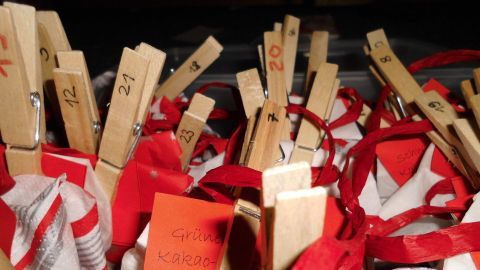 Ein Adventskalender zeigt 24 Teebeutel, die mit roten Bändern und Wäscheklammern nummeriert sind, in einer festlichen Umgebung.