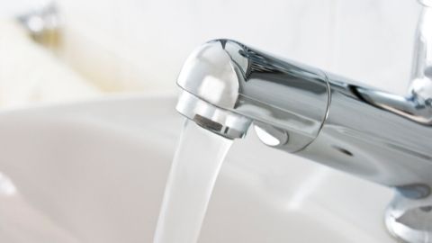 Ein glänzender Wasserhahn gibt Wasser ab, während er in einem modernen Badezimmer auf einer weißen Waschbeckenfläche steht.