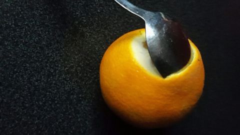 Eine orangefarbene Orange hat einen Löffel, der in die Frucht gesteckt ist, auf einem dunklen Untergrund.