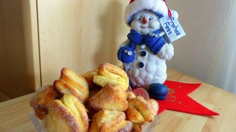Quarkplätzchen liegen auf einem gläsernen Teller, während eine Schneemannfigur mit roter Mütze daneben steht.