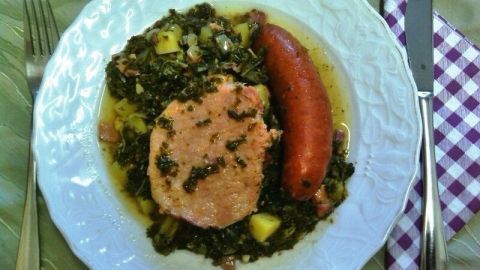 Ein Teller zeigt Grünkohl mit Kassler und einer Wurst, köstlich angerichtet auf einem Tisch mit Besteck.