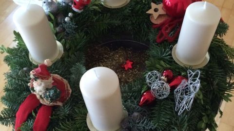 Ein Adventskranz mit vier weißen Kerzen, dekoriert mit roten und silbernen Ornamenten, steht auf einem Holzboden.